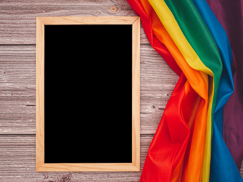 Top view of the rainbow flag or LGBT and a blank mini chalkboard with the wooden border over a cement floor with copy space. Flat lay