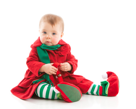 A cute baby girl, dressed as a Christmas elf, plays with jingle bells. Huge oversized elf shoes.