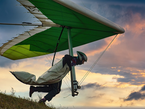 Hang glider pilot runs from the hill into sunset sky.