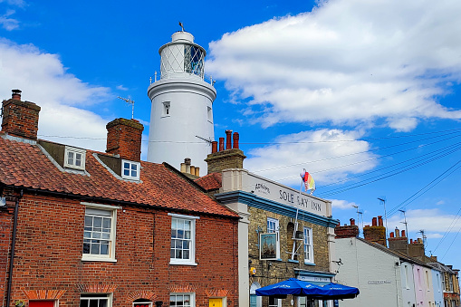 Southwold, Suffolk, England, UK - Adnams Sole Bay Inn pub between cottages in East Green Road, with lighthouse in background on a sunny summer day