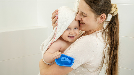Smiling mother wiping her baby son with towel after washing in bath. Concept of children hygiene, healthcare and parenting