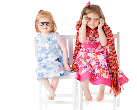 A full length image of  two sisters, a two year old and a three year old little girl sitting together playfully in dress up clothes. 