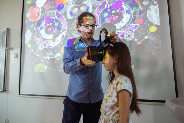 Lecture virtual reality and AI One professor helping his young student put on VR glasses teacher projector stock pictures, royalty-free photos & images
