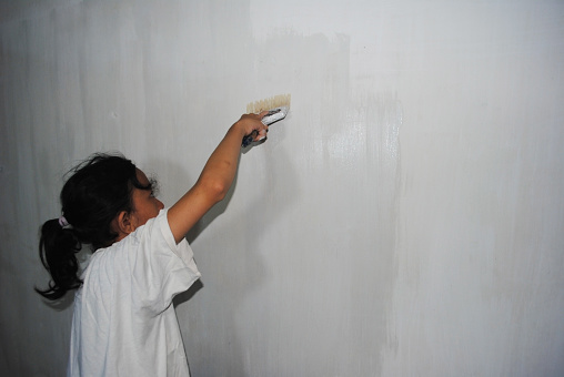 Indonesian girl is painting her own room in white color.