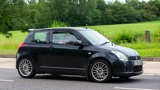 Milton Keynes,UK - Aug 13th 2023: Black 2006 Suzuki Swift  car driving on an English country road.