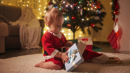 Cute baby playing with Christmas gift box under decorated Christmas tree. Families and children celebrating winter holidays