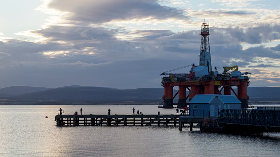 People fishing from the pier at Cromarty, Scotland, near to an oil rig which is being decommissioned.