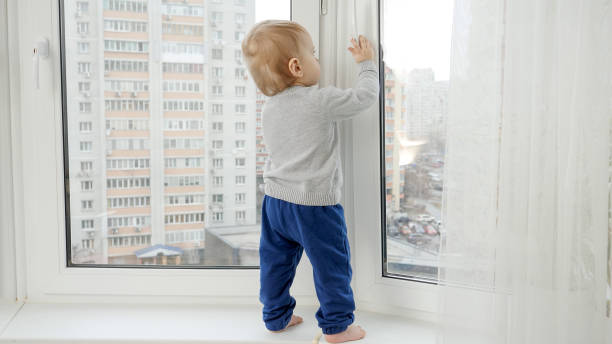 istock Little baby boy standing on windowsill and pulling window handle. Baby in danger. CHild safety. 1612040974