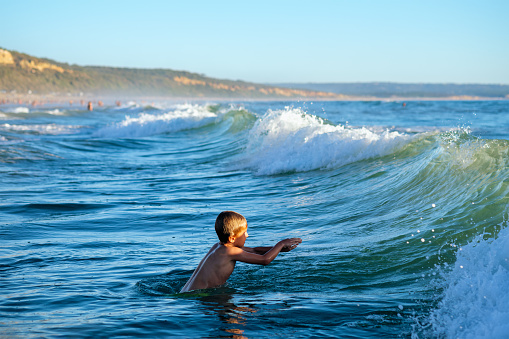 Boy has fun enjoys jumps dives in ocean sea waves of Atlantic Ocean. Fonta da Telha beach, Costa da Caparica, Portugal