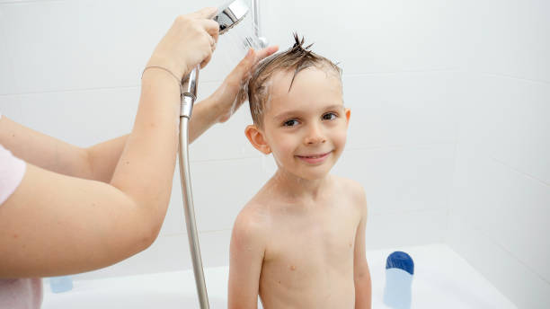 istock Young smiing boy looking in camera while mother washing his head in shower 1612097772