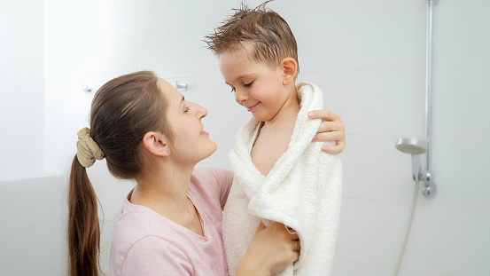 Caring mother drying her son with towel and hugging after bathing. Concept of hygine, children development and fun at home.