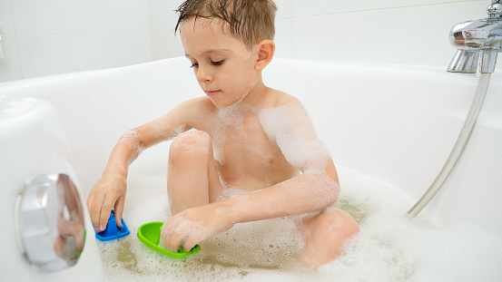 Cute boy washing in bath and having with plastic toys. Concept of family time, children development and fun at home.