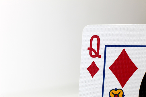 A macro photo of the Queen of Diamonds playing card, showing the texture of the card, set against a pale background.