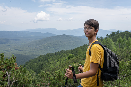 Teenager hiking in the high mountains of Slovenia from Pokljuka to Viševnik, walks up, conquers the top of the mountain, enjoys the views of the forests of Pokljuka, the Julian Alps, enjoys the conquered peak of Viševnik