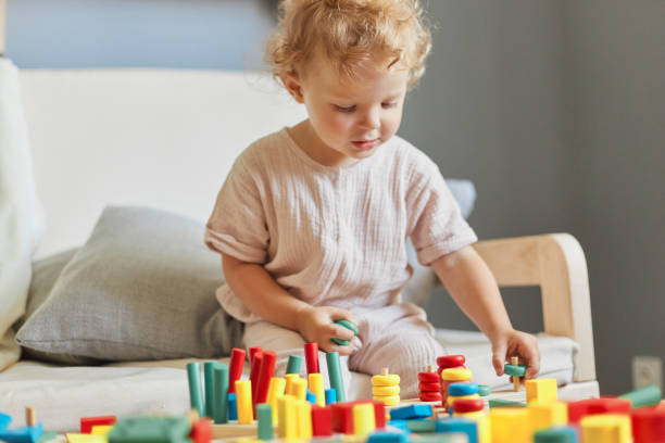 istock Learning through colorful play. Little nursery exploration. Playground fun and games. Charming wavy haired blonde toddler baby playing wooden educational toys at home interior. 1612171835