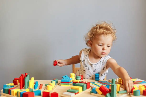 istock Childhood curiosity and discovery. Playful games for curious minds. Cute creative wavy haired blonde toddler baby playing wooden educational toys isolated over gray background 1612171863