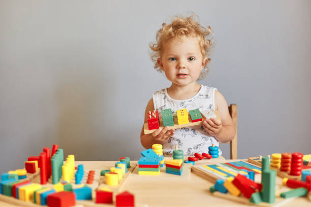 istock Infants' joyful learning experiences. Toddler's curious exploration. Child's imaginative playtime. Funny wavy haired blonde toddler baby playing wooden educational toys isolated over gray background 1612171868