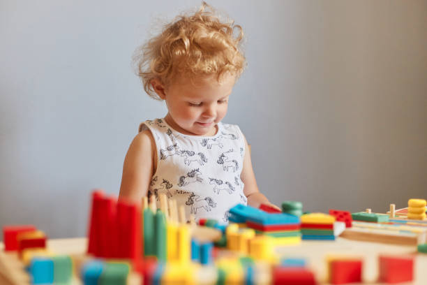 istock Exploring colorful educational activities. Infants' joyful learning experiences. Child's imaginative playtime. Charming wavy haired blonde infant baby playing wooden educational toys against gray wall 1612171876