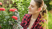 Beautiful smiling brunette woman working in her domestic garden and growing pink roses
