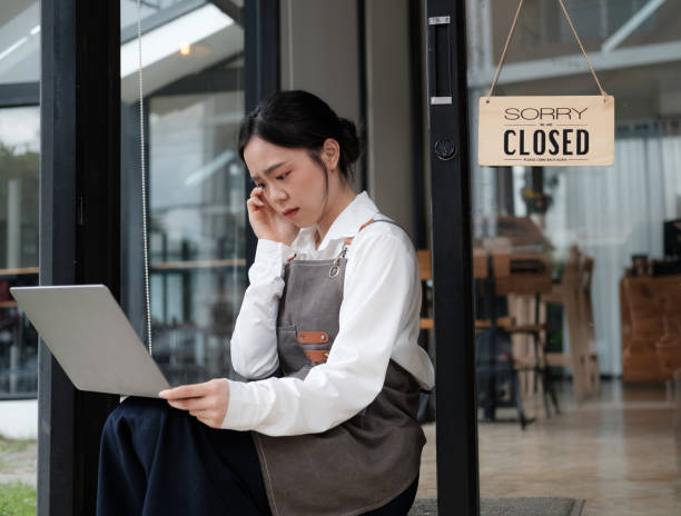 Young and depressed coffee shop owner tuning the closed sign, shutting down her cafe in crisis. Young and depressed coffee shop owner tuning the closed sign, shutting down her cafe in crisis. chief of staff stock pictures, royalty-free photos & images