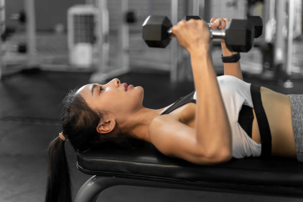 istock Attractive young woman lifting a small dumbbell in each hand while laying on a workout bench in a fitness gym 1612245549