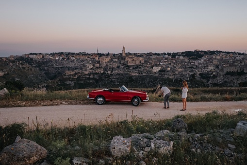 Matera, Italy – July 26, 2023: 1962 Alfa Romeo Spider in red with Matera, Italy in the background with two people