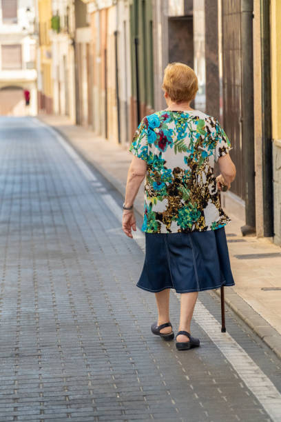 View from behind of an older woman walking with a cane down the cobbled street of the village
