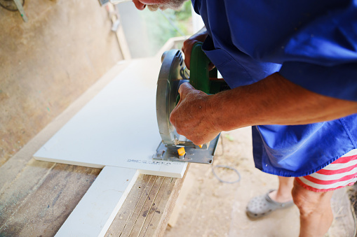 an elderly man in goggles with a circular saw. A circular saw is an indispensable tool in the manufacture of chipboard furniture.