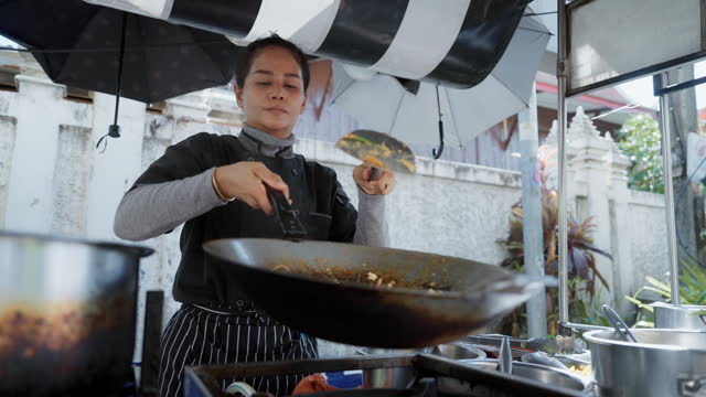 Close-up woman chef adding ingredients of Pad Thai in hot pan and Pad Thai most famous street food in Bangkok Thailand.