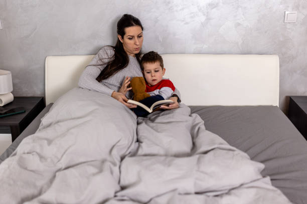 istock A young mother is reading a book with her son in a bedroom. 1612340700