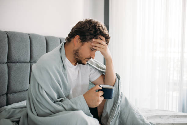 istock Man sitting on the bed with blanket trying to get up 1612345025