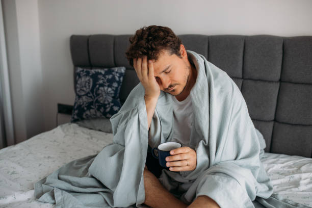 istock Man sitting on the bed with blanket trying to get up 1612346606
