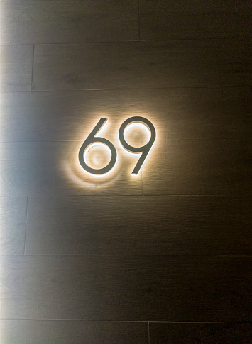House number 69 backlit with wood effect tile background. Houses with personality concept