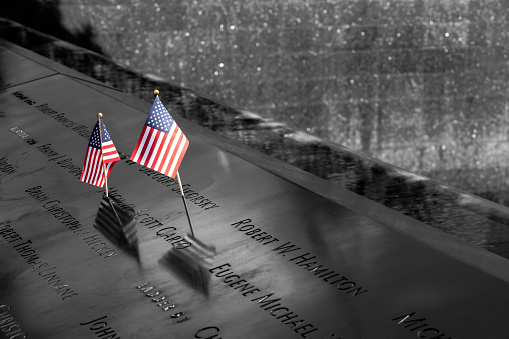 Two American flags adorn a plaque full of names of some of those who died in the 9/11 attacks in New York City, USA. Selective Colour.