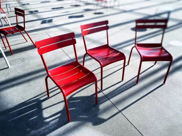 Three red chairs in the afternoon sun with dramatic shadows.