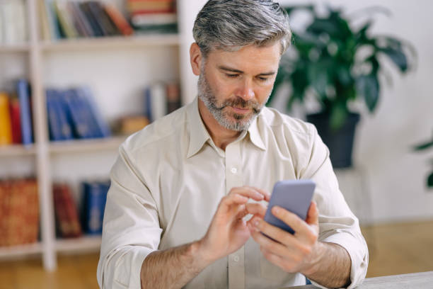 istock Serious elderly middle-aged man using applications on the phone relaxes, works while sitting at home. 1612473144