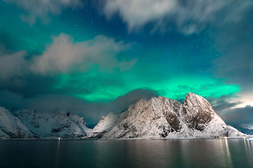 Beautiful northern lights over snowy mountains at the sea in winter. Sakrisoy, Lofoten