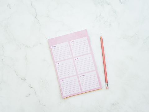 Pink blank planner sheet and pencil on white marble background. Mockup of weekly planner. Flat lay, top view, mock up, concept