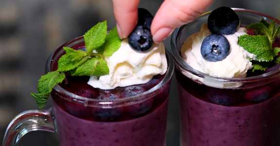 decorate dessert with blueberries berries stick into cream in two glass glasses on a dark background mint leaves delicious jelly dessert. gelatin is good for joints