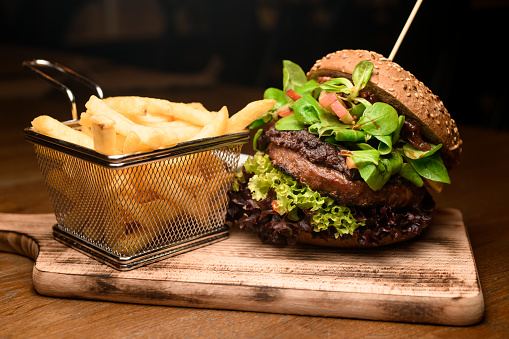 great appetizing view on big tasty double burger with fresh green lettuce and spinach and French fries on a wooden board