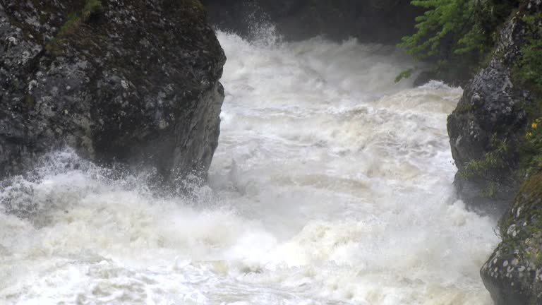 Super slow motion footage of dangerous flood waters flowing in river through big rocks