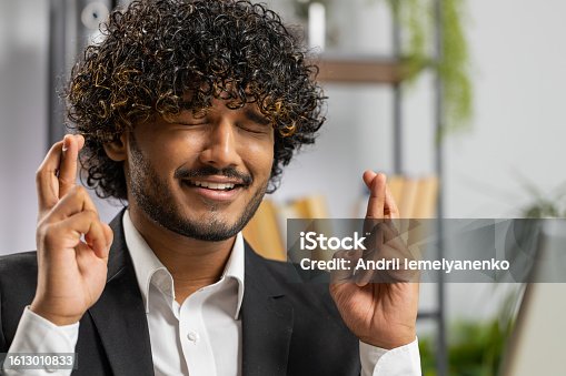istock Indian businessman crossed fingers looking at laptop screen asking for good luck news win victory 1613010833