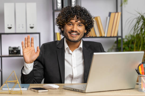 istock Businessman working on laptop smiling friendly at camera and waving hands gesturing hello at office 1613011353