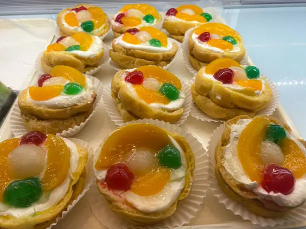 Photo of row of decorated cakes in a glass case, with fruit topping on it