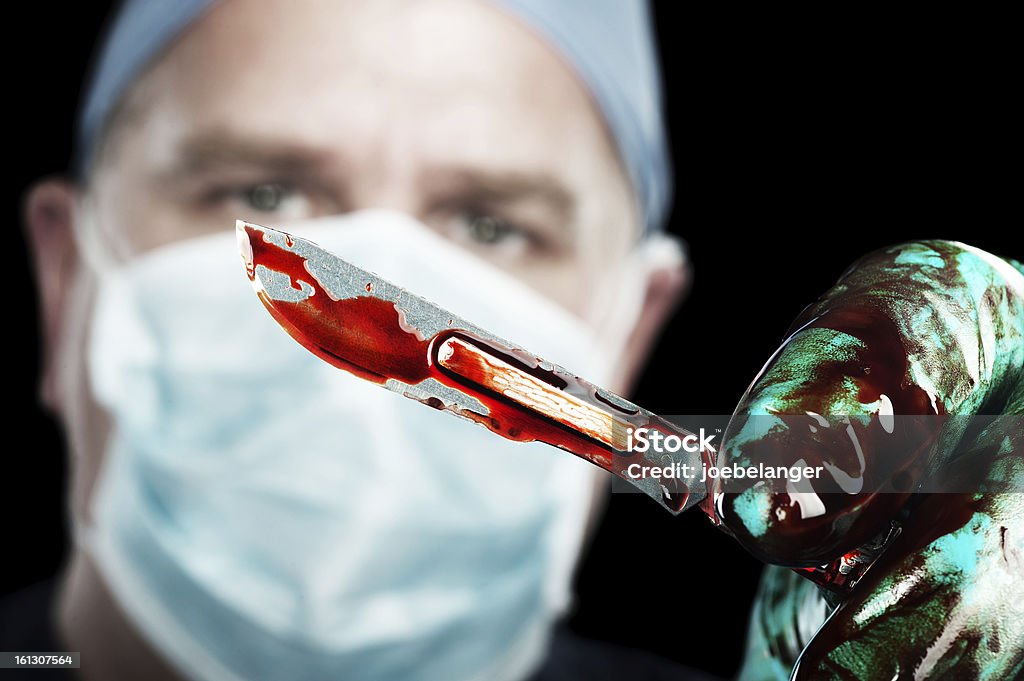 Surgeon with scalpel A male surgeon holds up a sharp, bloody scalpel during surgery Blood Stock Photo