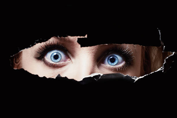 Blue eyes of a young woman peeping through a hole