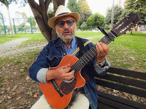 senior man playing guitar on park bench