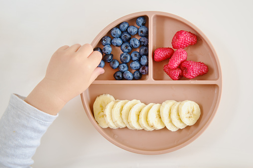 The toddler baby hand closeup shows him enjoying a snack of fresh fruits and berries. Kid boy aged two years (two-year-old)