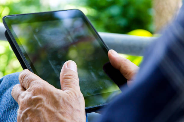 istock Senior man sitting outside reading E-book on his tablet. 1613231637