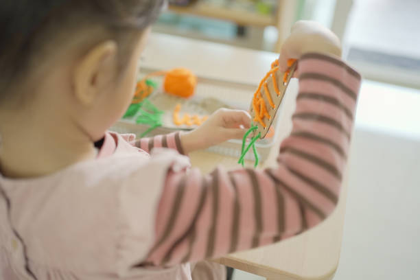 istock Preschool mixed girl threading a carrot shaped sewing card 1613283709